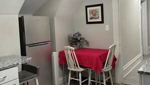 A compact kitchen with a dining area, a refrigerator, a table with chairs, and a ceiling light fixture. - The Yellow-Shuttered House apt B (Sharon)