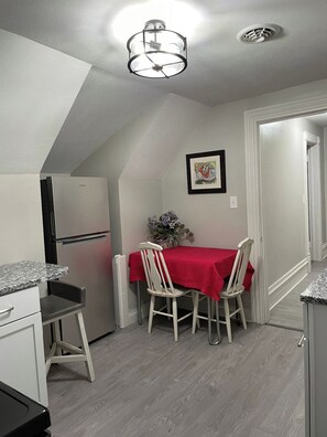 Ett kompakt kök med en matplats, ett kylskåp, ett bord med stolar och en taklampa.