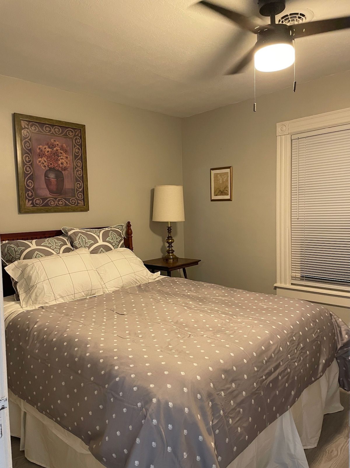 Quarto com cama, ventilador de teto, luminária na parede e janela com persianas.