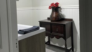 A room with a wooden cabinet, a dark wooden table with a vase of red flowers, and a white radiator. - The Yellow-Shuttered House apt B (Sharon)
