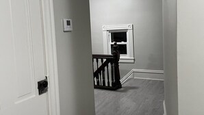A hallway with a white door, a small window, and a staircase with a wooden railing. - The Yellow-Shuttered House apt B (Sharon)