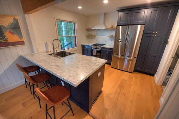 A kitchen with a marble island, dark cabinets, stainless steel appliances, and wooden flooring.