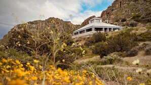 A modern building with a flat roof and large windows, surrounded by a natural landscape with yellow flowers and rocky hills. - Spacious Artist Loft  in Tehachapi (Tehachapi)