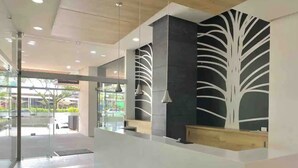 A modern reception area with a glass entrance, a reception desk, and a wall with a tree-like design. - LUXURY APARTMENT IN THE GOLDEN MILE OF IBAGUÉ, COLOMBIA. (Ibagué)