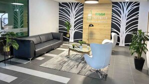 A modern lobby with a black leather sofa, a glass coffee table, a blue armchair, and a wooden accent wall with a tree design. - LUXURY APARTMENT IN THE GOLDEN MILE OF IBAGUÉ, COLOMBIA. (Ibagué)
