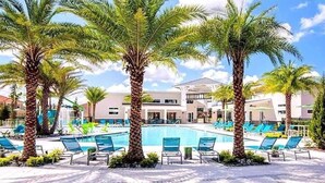 A pool area with palm trees, lounge chairs, and a building with a modern design.