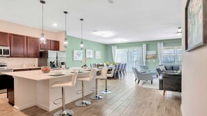 A modern kitchen with a central island, bar stools, and a dining area with a table and chairs.