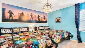 Une chambre avec deux lits, chacun recouvert d’une couette à motifs de super-héros. Un grand mur est décoré d’une fresque représentant des super-héros, et la pièce est également dotée d’un lustre et d’une fenêtre ornée de rideaux à motifs d’étoiles.