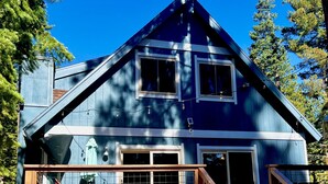 A two-story house with a porch, a staircase, and a fenced area with a blue play structure. - Iconic modern A-frame steps from lake and pet friendly (Carnelian Bay)