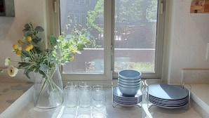 A kitchen counter with a vase of flowers, a stack of plates, and a window with a view of trees. - Iconic modern A-frame steps from lake and pet friendly (Carnelian Bay)