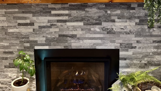 A fireplace with a stone wall backdrop, a wooden shelf with books and a plant, and a potted plant beside the fireplace. - Iconic modern A-frame steps from lake and pet friendly (Carnelian Bay)