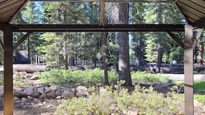 A covered outdoor seating area with a bench and a log table, surrounded by a forested landscape. - Iconic modern A-frame steps from lake and pet friendly (Carnelian Bay)
