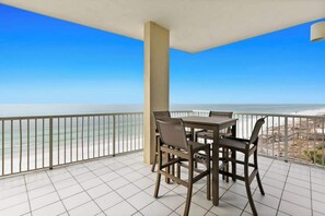 A balcony with a view of the ocean, a table with chairs, and a tiled floor.