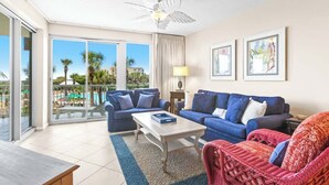 A hotel room with a balcony, two blue sofas, a red wicker chair, a coffee table, and framed artwork on the wall. - The Crescent 105 (Miramar Beach)