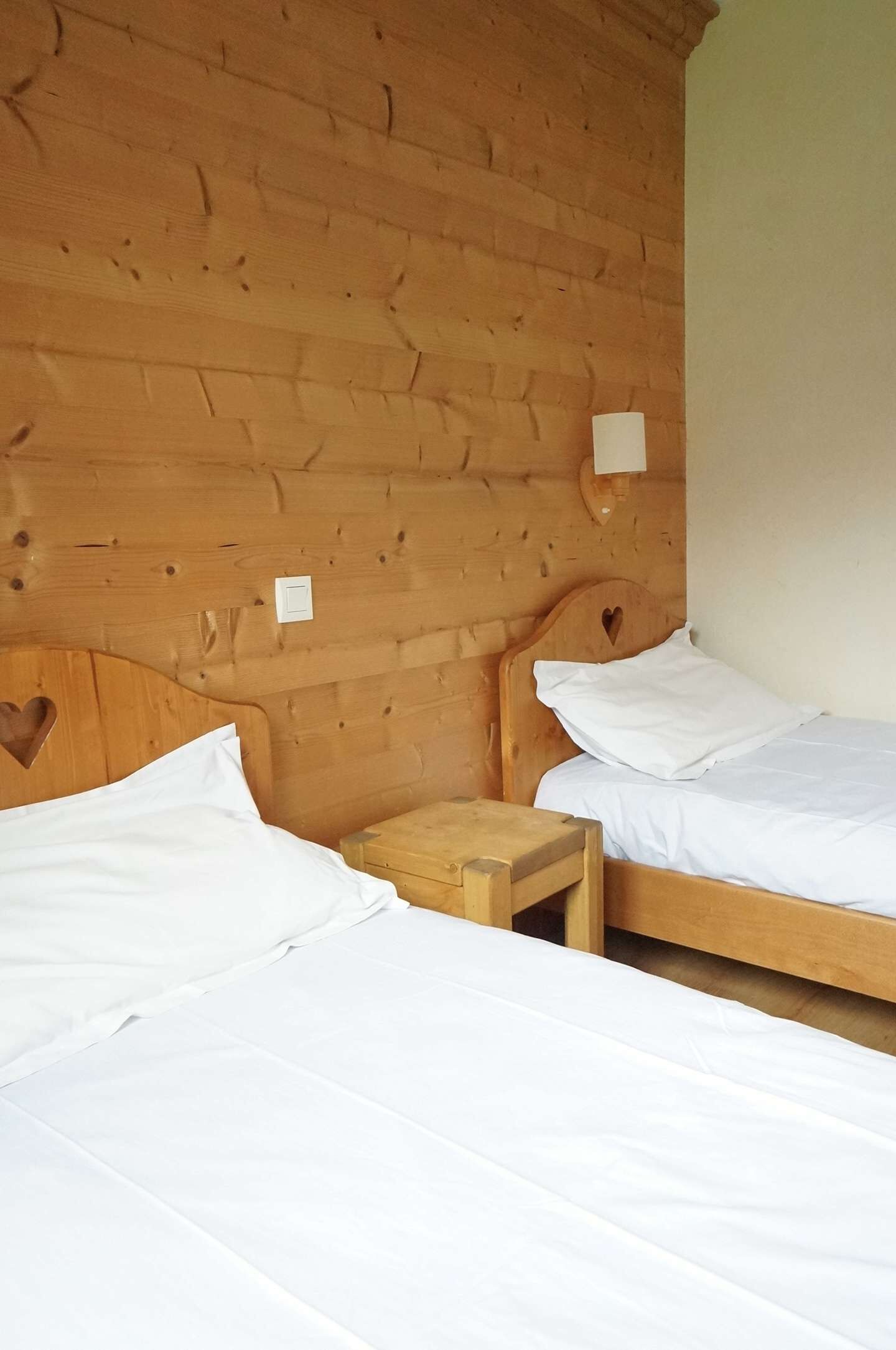 A room with two wooden beds, each with a heart-shaped cutout on the headboard, and a small wooden nightstand between them.