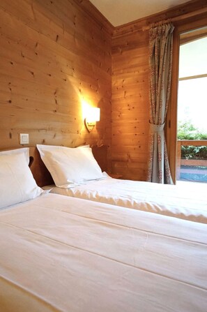 Una habitación de cabaña de madera con una cama, una lámpara fijada a la pared y una ventana con cortinas.