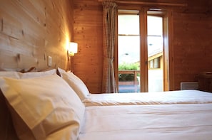 Una habitación de cabaña de madera con cama, mesita de noche y ventana con cortinas.