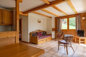 Un interior de cabaña acogedor con vigas de madera, un sofá, sillas de mimbre, un televisor y una mesa de comedor.