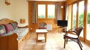 A cozy room with a wooden sofa, a small table, and a TV. - Rés Aravis C19 : Pistes et Cœur de Village à 3 min à Pied + Terrasse et Vue (LE GRAND BORNAND)