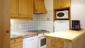 A kitchen with wooden cabinets, a microwave, a coffee maker, a stove, and a dishwasher. - Rés Aravis C19 : Pistes et Cœur de Village à 3 min à Pied + Terrasse et Vue (LE GRAND BORNAND)
