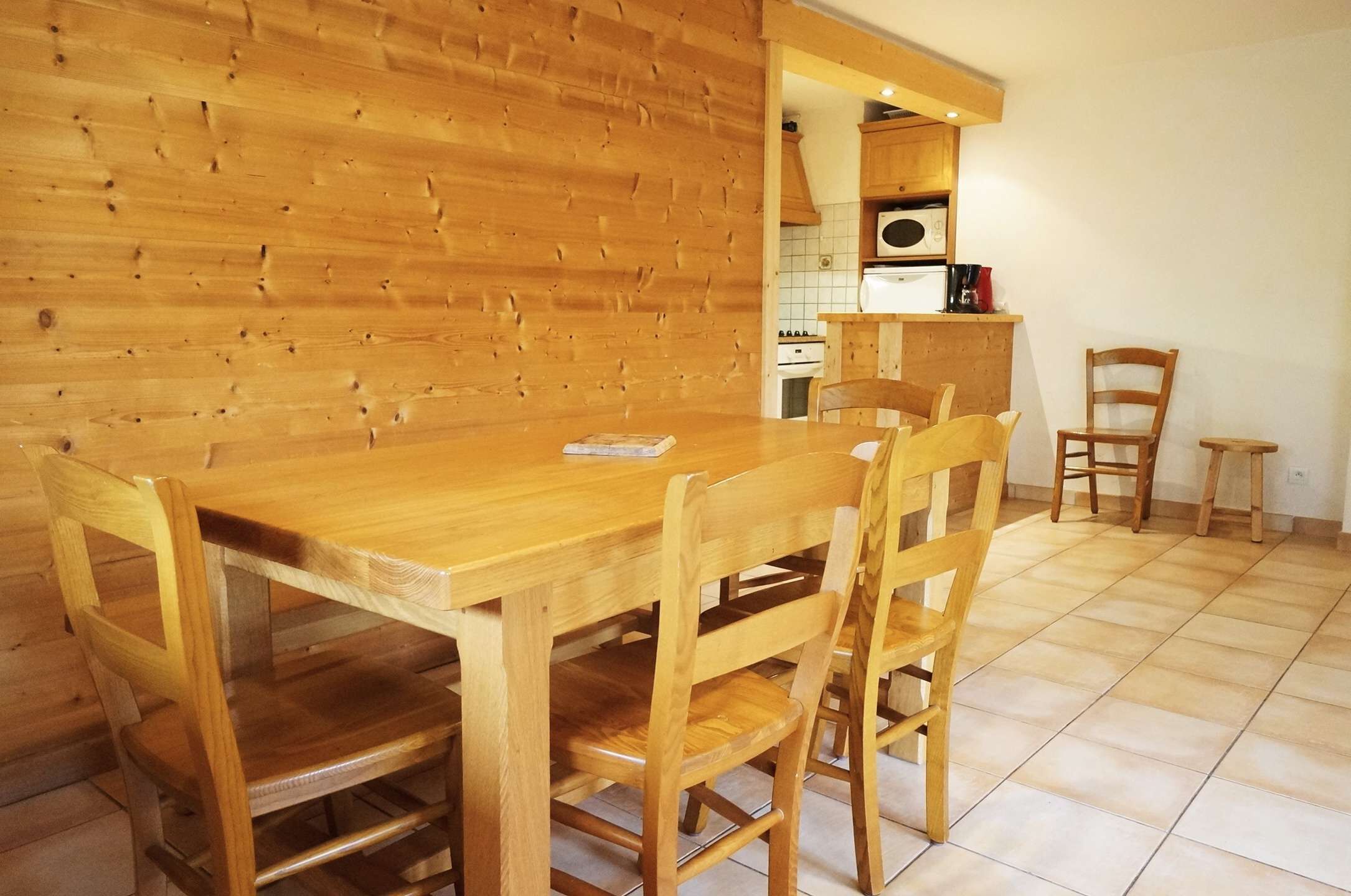Een houten eettafel met vier stoelen in een kamer met houten wanden en betegelde vloer.