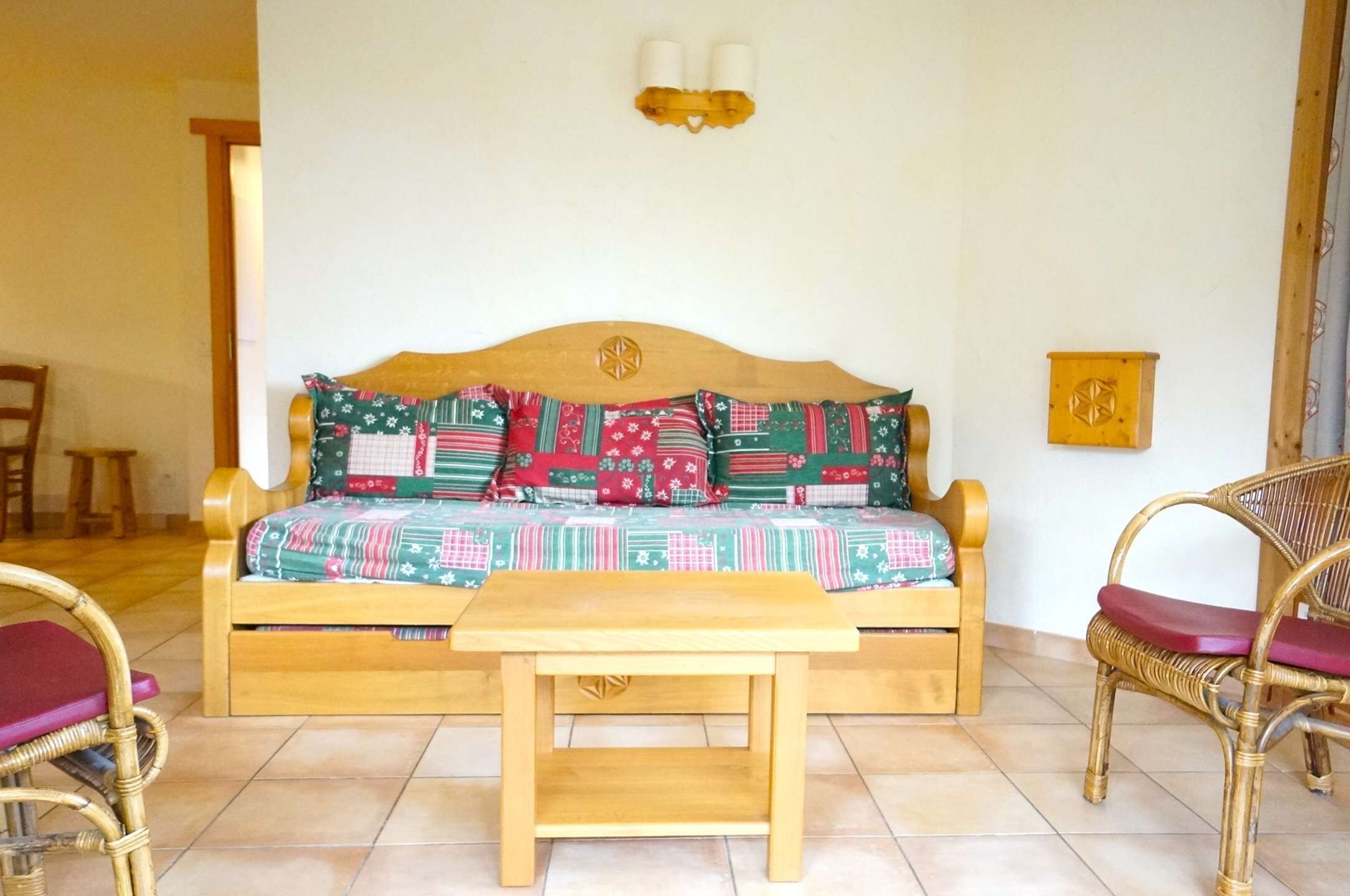 A cozy room with a wooden sofa, two wicker chairs, a small wooden table, and a wall-mounted light fixture.