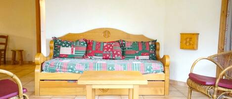 A cozy room with a wooden sofa, two wicker chairs, a small wooden table, and a wall-mounted light fixture.