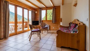 A wooden interior with a sofa, two wicker chairs, a TV, and large windows offering a view of the outdoors.
