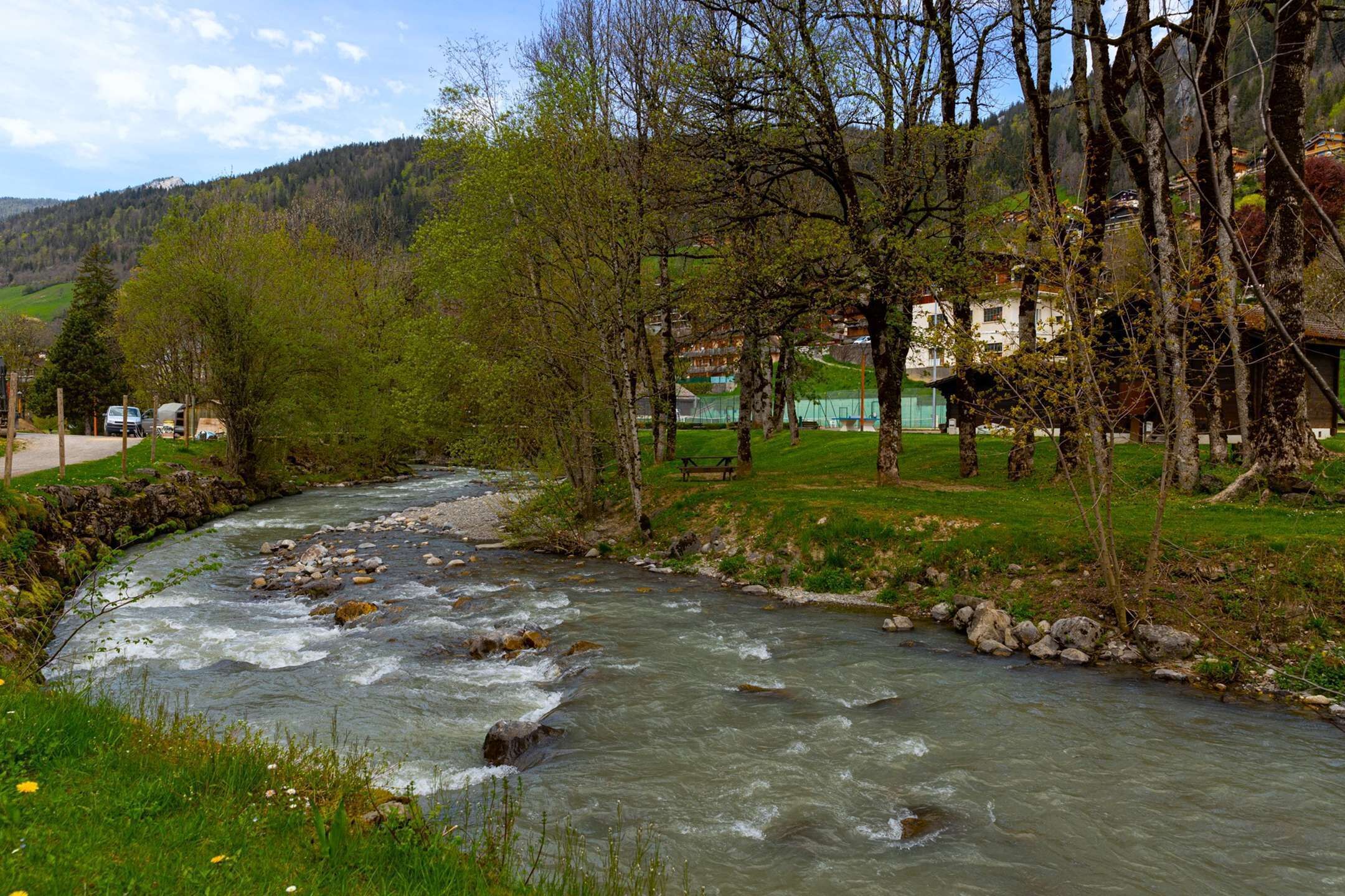 A river flowing through a valley with a picnic table and a stone wall on the bank.
