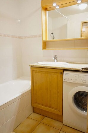 Ein Badezimmer mit Holzschrank, weißem Waschbecken, Spiegel, Badewanne und einer Waschmaschine mit Frontlader.