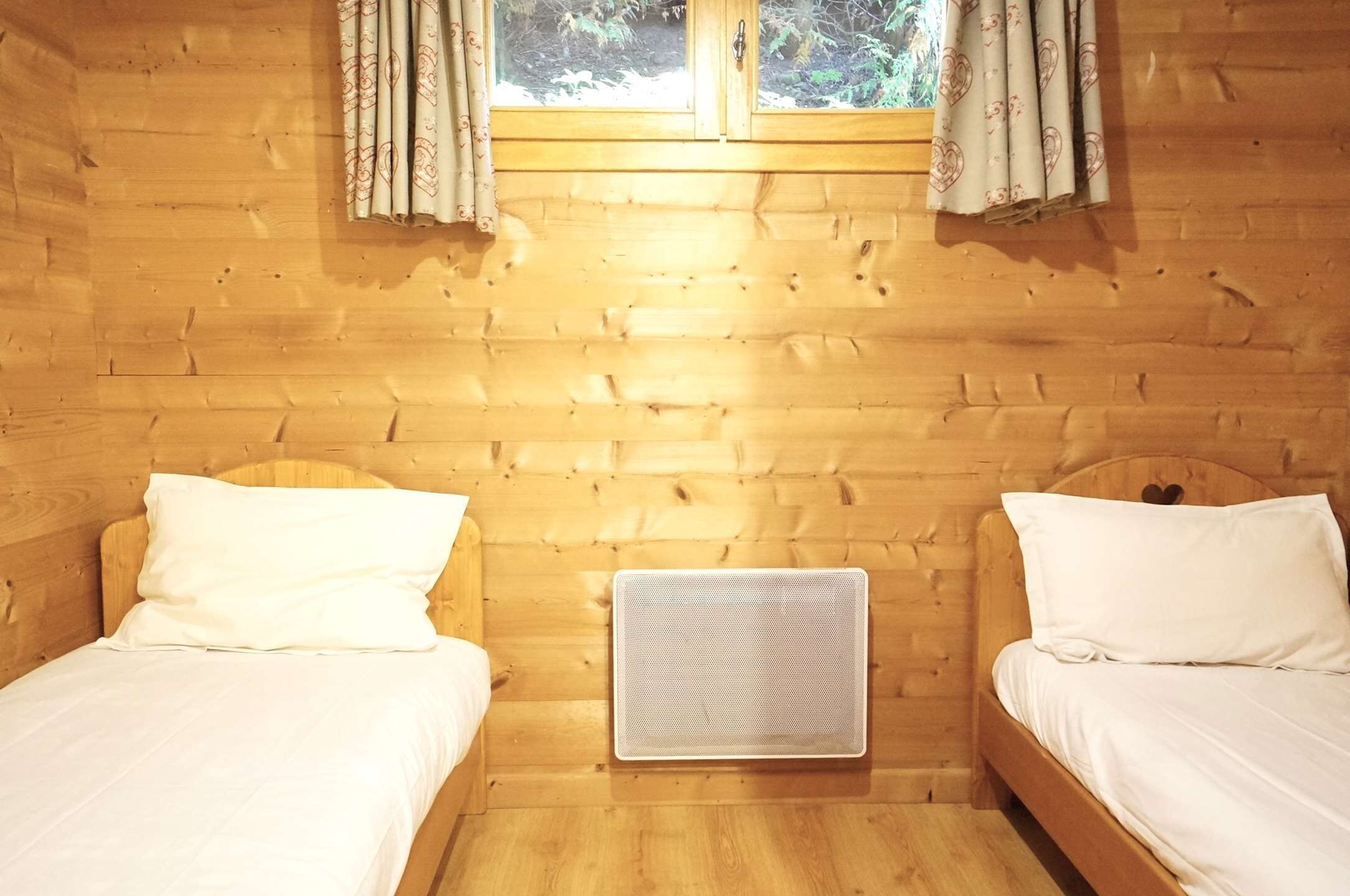 A wooden cabin room with two beds, a window with curtains, and a wall-mounted air conditioner.