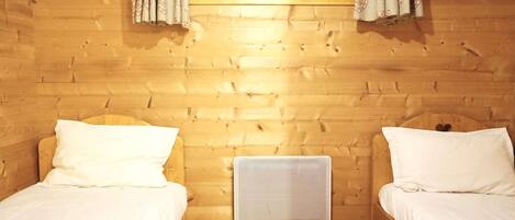 A wooden cabin room with two beds, a window with curtains, and a wall-mounted air conditioner.
