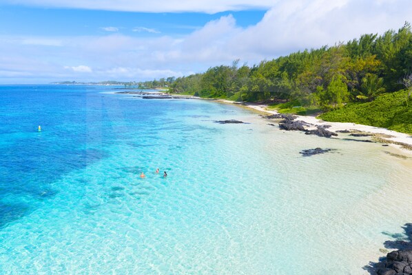 Une plage à l’eau turquoise et limpide, bordée d’un rivage sablonneux et d’une végétation luxuriante.