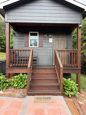 A wooden cabin with a porch, a welcome mat, and a sign indicating a fire safety feature.