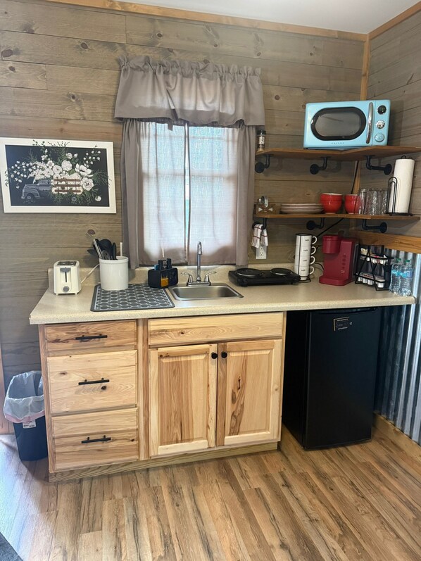 A compact kitchen with wooden cabinetry, a built-in microwave, a coffee maker, and a sink.