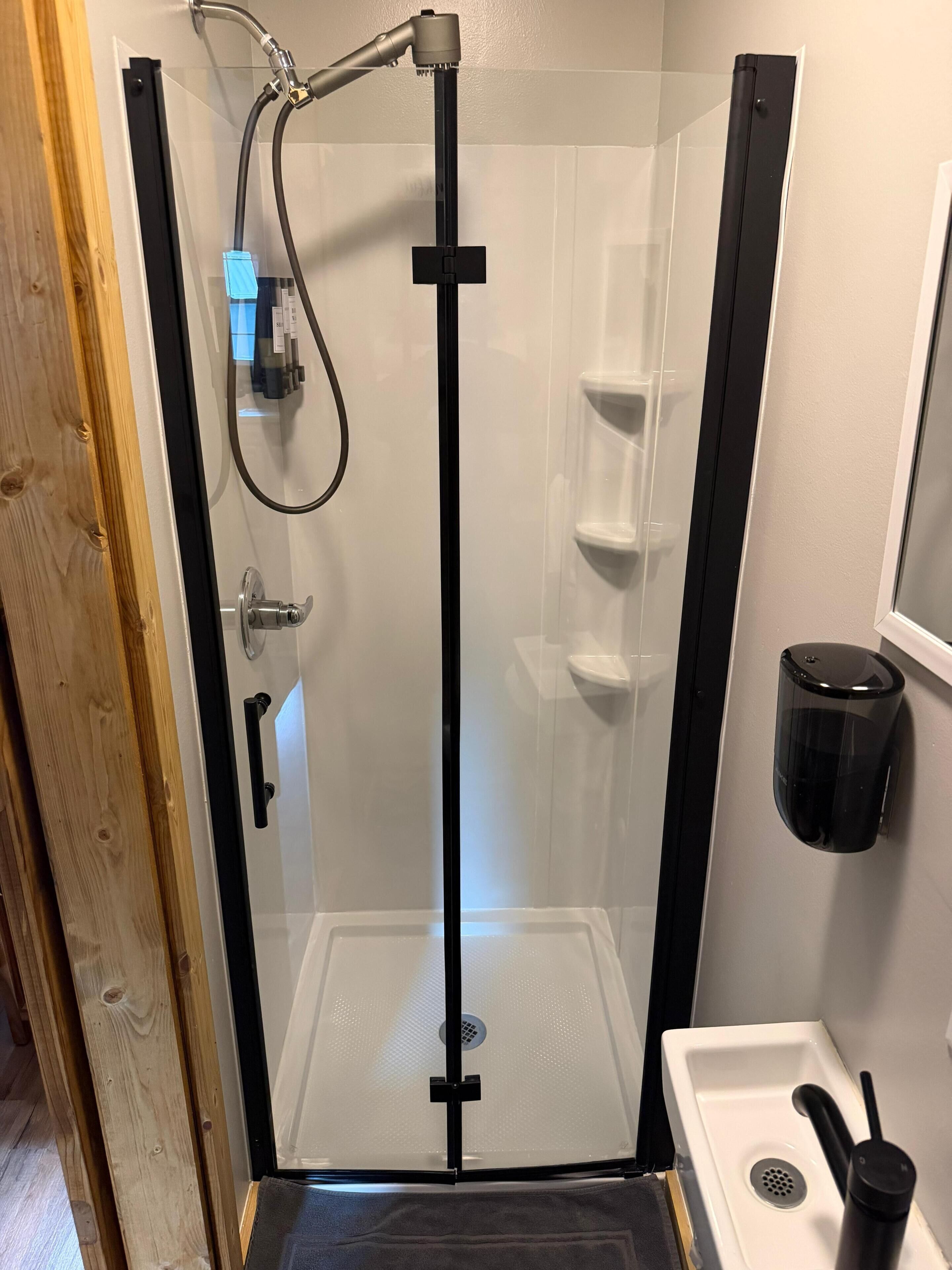 Eine Duschkabine mit Glastür, Handbrause und Wandseifenspender.