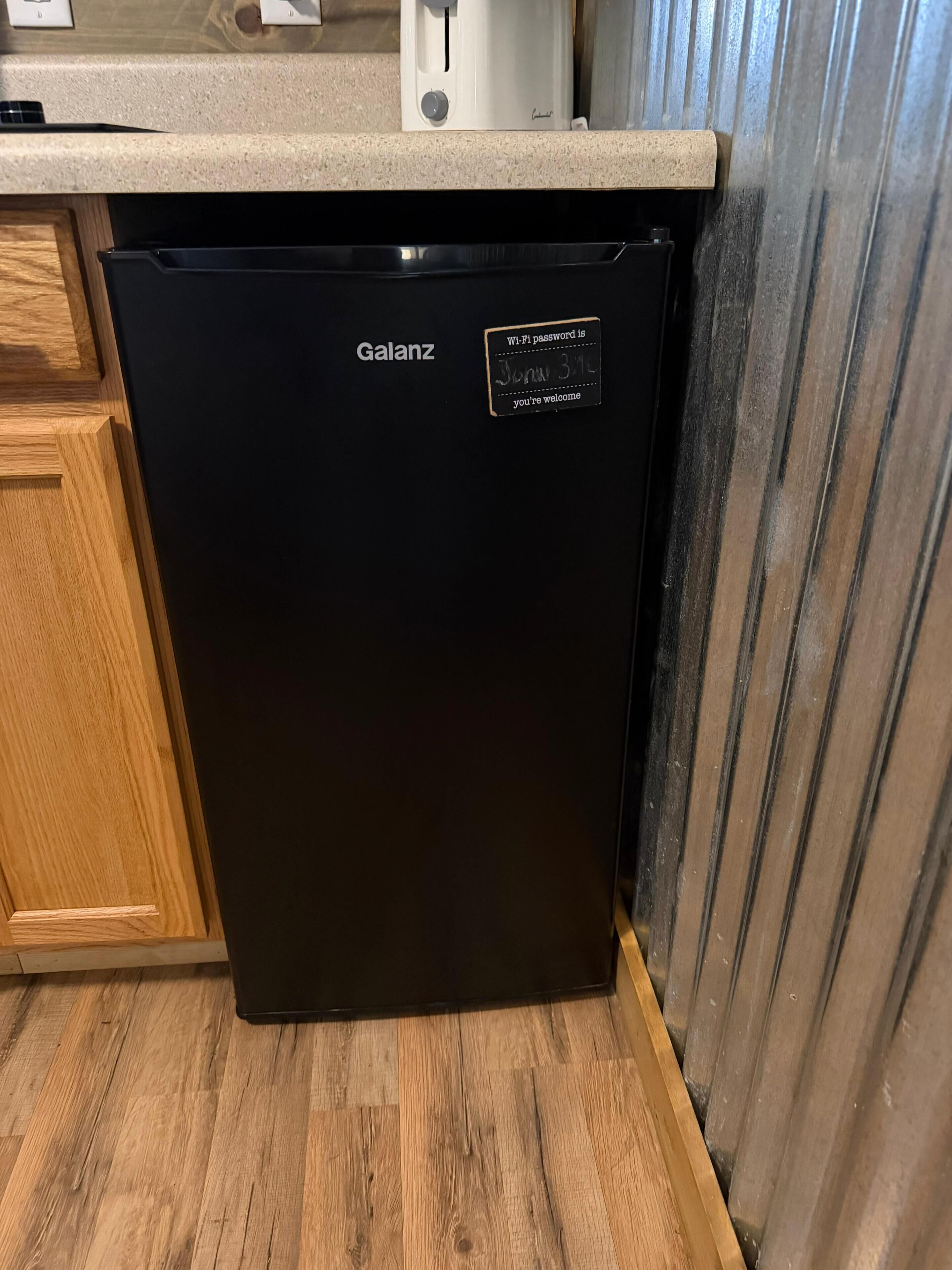 A black Galanz refrigerator in a kitchen with wooden cabinets and a countertop.