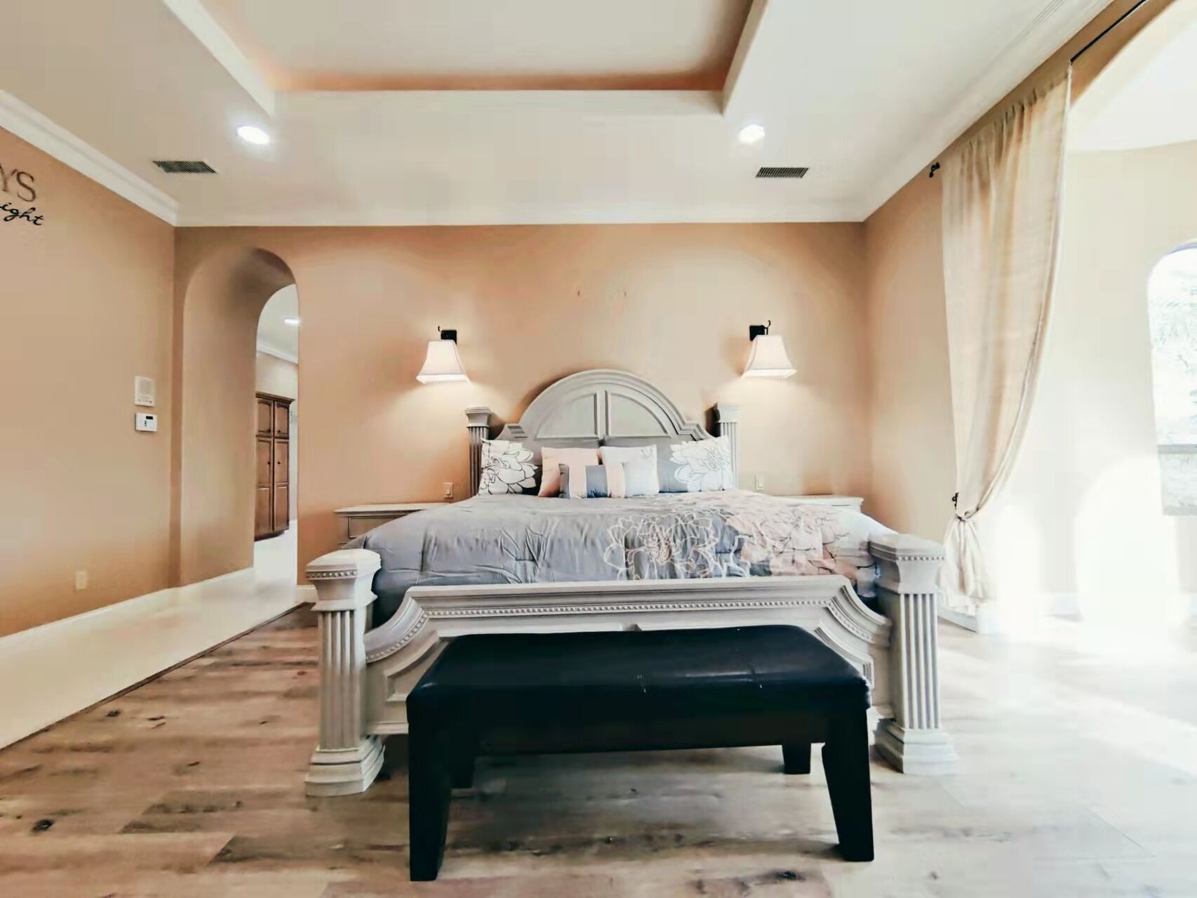 Quarto com uma cama grande, duas luminárias de cabeceira, um banco e vista para o exterior pela janela.