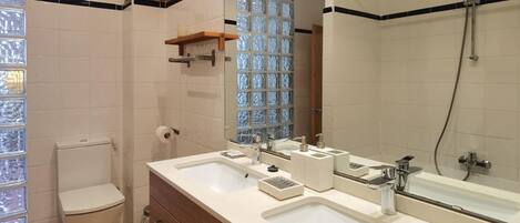 A modern bathroom with two sinks, a toilet, a shower, and a large mirror.