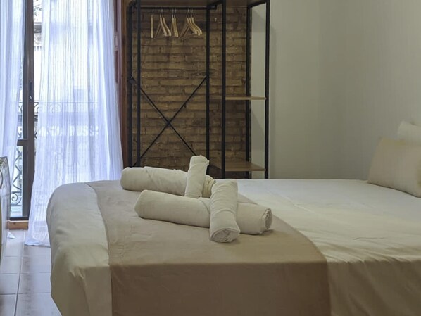 A neatly made bed with rolled towels, a brick wall, and a metal rack with clothes. - Enjoy a 2-room apartment. Apartment in Ruzafa with a very sunny terrace (Valencia)