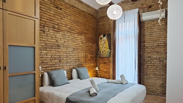 Ein Schlafzimmer mit Backsteinwand, einem Bett mit weißer Bettwäsche und grauen Kissen, einem Holzschrank, einem Gemälde und einer Klimaanlage.