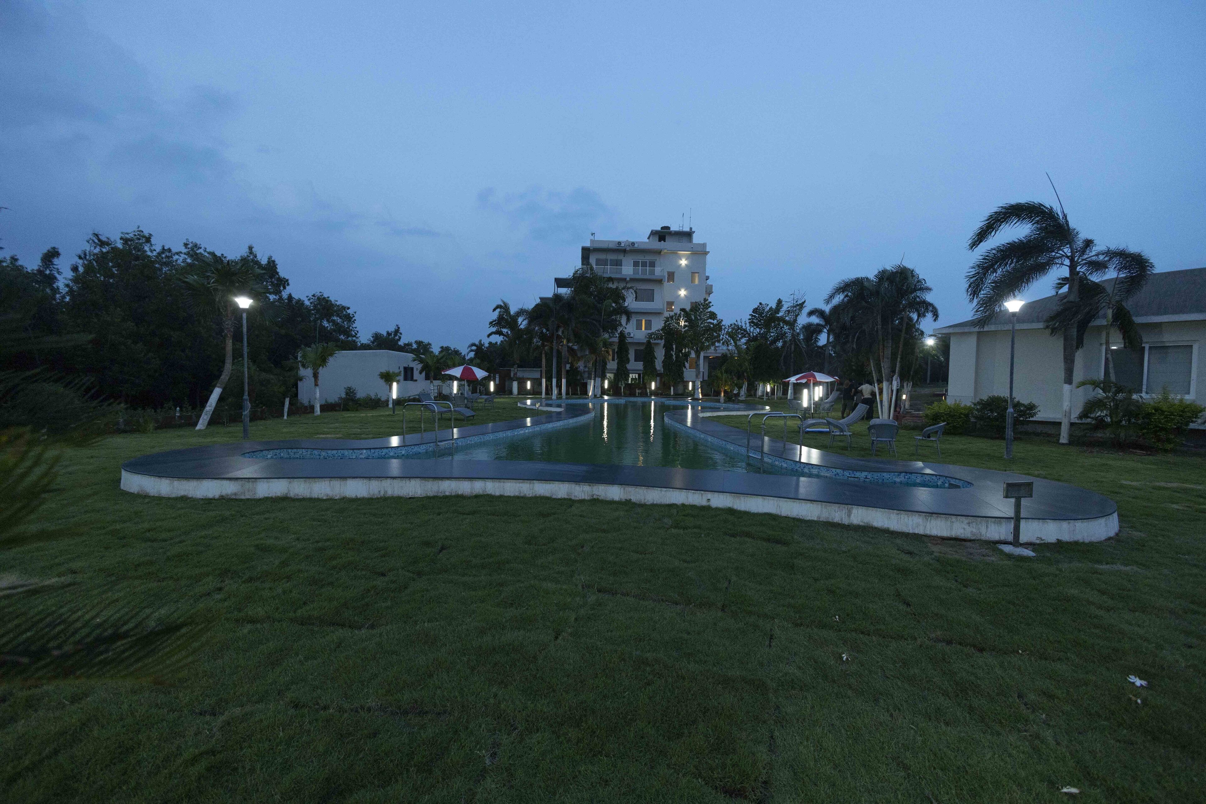 A pool area with a circular design, surrounded by grass and palm trees, with a building in the background.