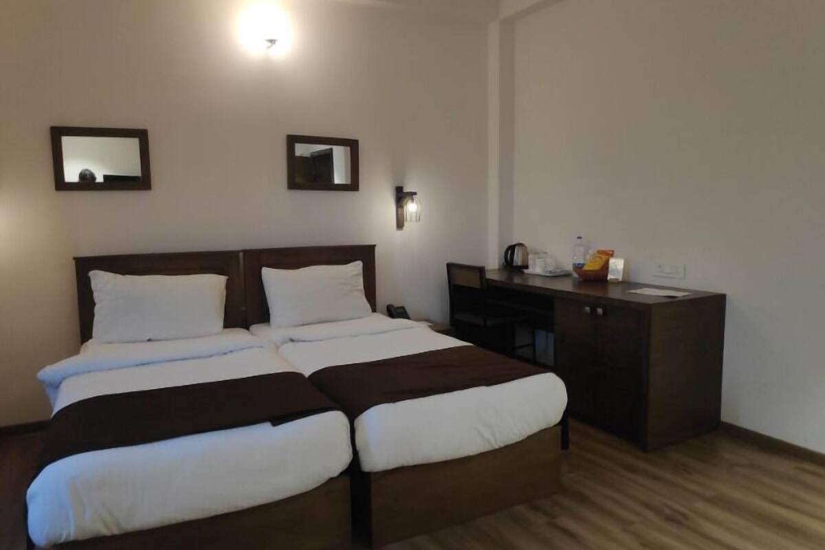 A double bed with a wooden headboard, a bedside table, and a desk with a chair. There are two wall-mounted light fixtures and a mirror above the bed.