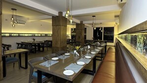 A modern restaurant with long communal tables, wooden pillars, and hanging pendant lights. - SAMUDRA RESORTS AND SPA (Brahmagiri)