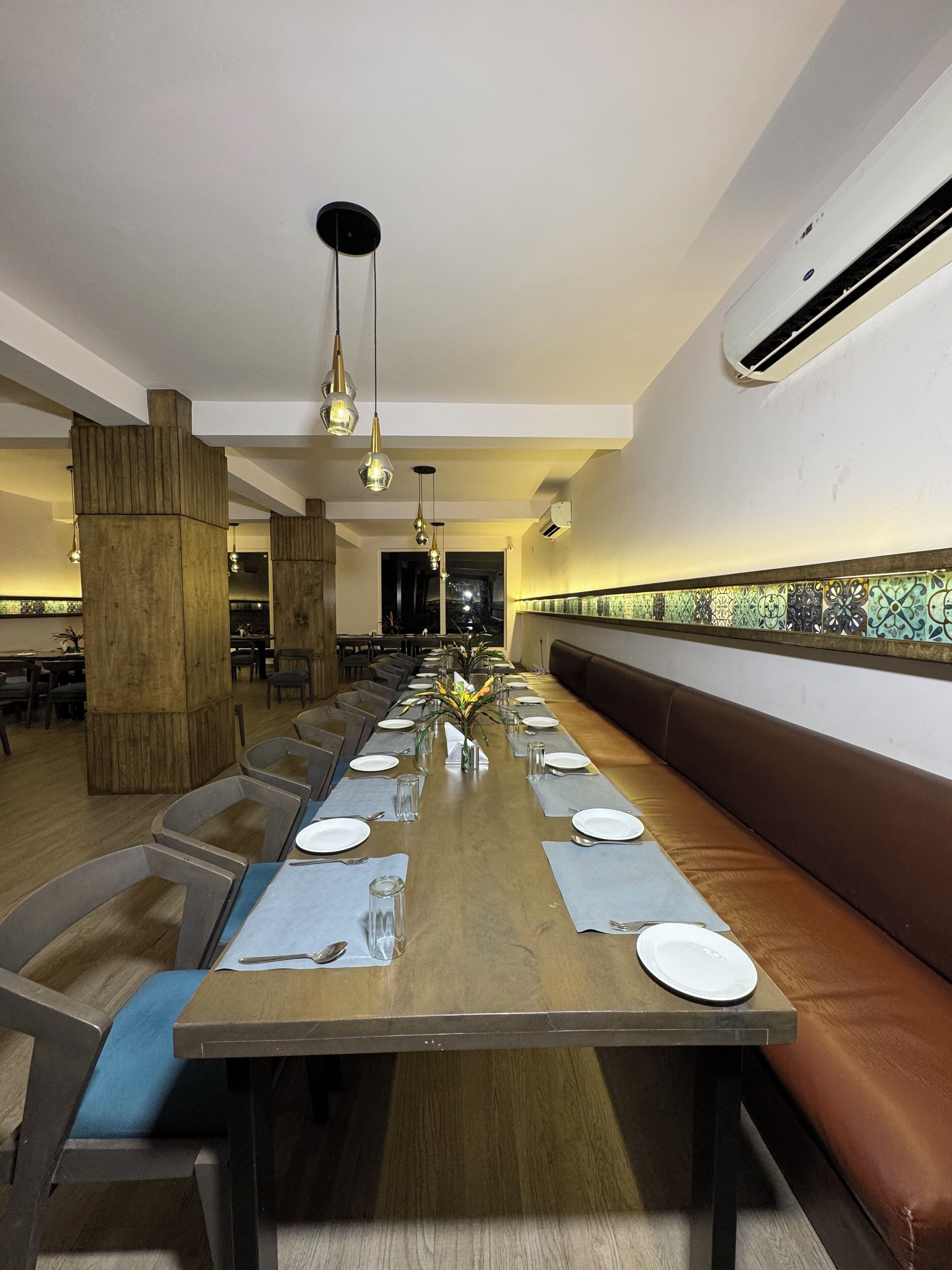 A long dining table with multiple chairs, a central floral arrangement, and a patterned wall backsplash.