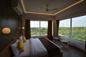A modern hotel room with a large bed, a balcony with a view, and a ceiling fan.