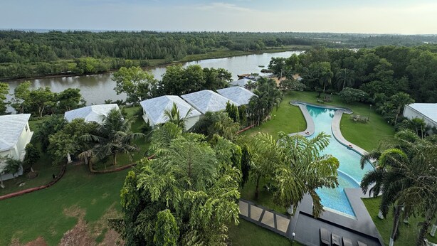 A resort with a swimming pool, lush greenery, and a river in the background. - SAMUDRA RESORTS AND SPA (Brahmagiri)