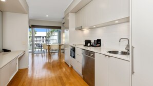 A modern kitchen with white cabinets, a stainless steel sink, and a dining area with a table and chairs. - The Sand Resort Kingscliff - One Bed (8308) (Tweed)