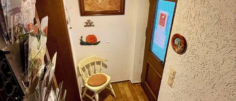 A small, cozy room with a wooden ceiling, a framed picture, a small table with a chair, and a digital display on the wall.