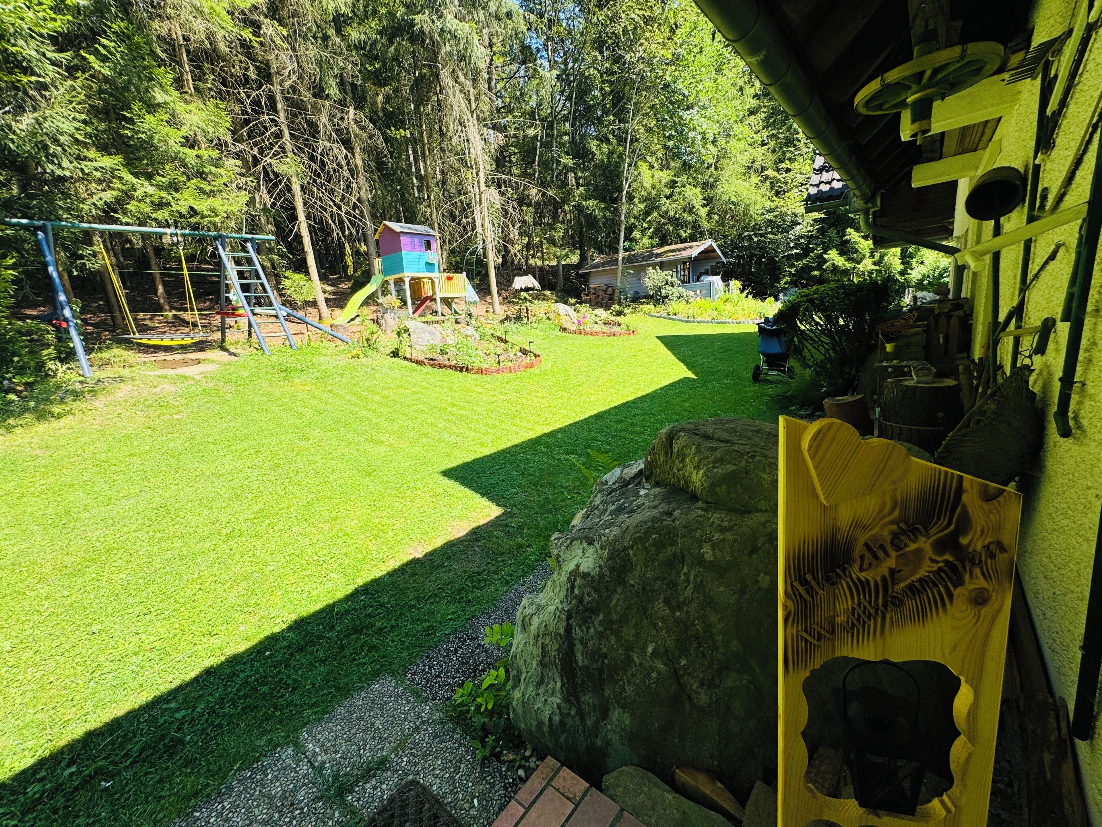 Ein Garten mit Schaukel, einer kleinen Spielhütte und einem Gartenbereich.
